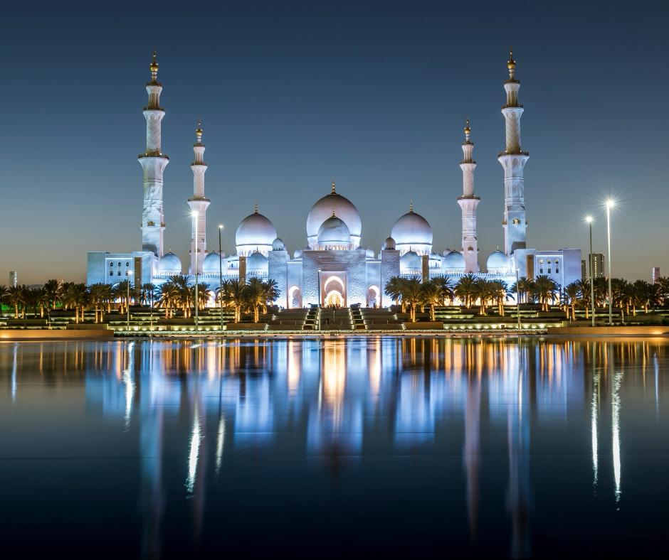 Picture of the Sheikh Zayed Grand Mosque in Abu Dhabi, United Arab Emirates. The photo is captured at dusk, showcasing its extensive illumination and reflection in the surrounding water features.